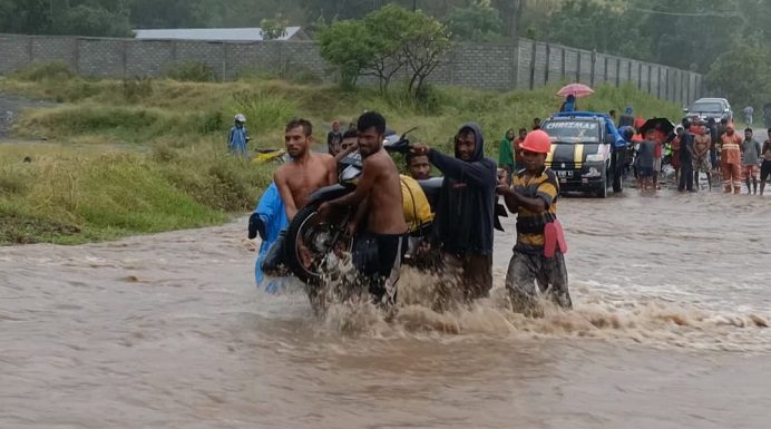 Banjir, Warga Alor Pikul Kenderaan Seberang Jalan Nasional Pemuda Desa Lembur sedang memikul kenderaan roda dua akibat banjir di jalan Nasional Kalabahi - Maritaing, Jumat (2/4/2021) siang.