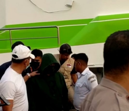 Polisi Tangkap Vikaris Gereja yang Perkosa 6 Anak di Alor Foto: Vikaris SAS (tengah jaket hitam tutup kepala) dikawal aparat Polres Alor setelah tiba di pelabuhan Kalabahi, Senin (5/9) sekitar pukul 17.00 WITA. (Foto: doc tribuanapos.net).
