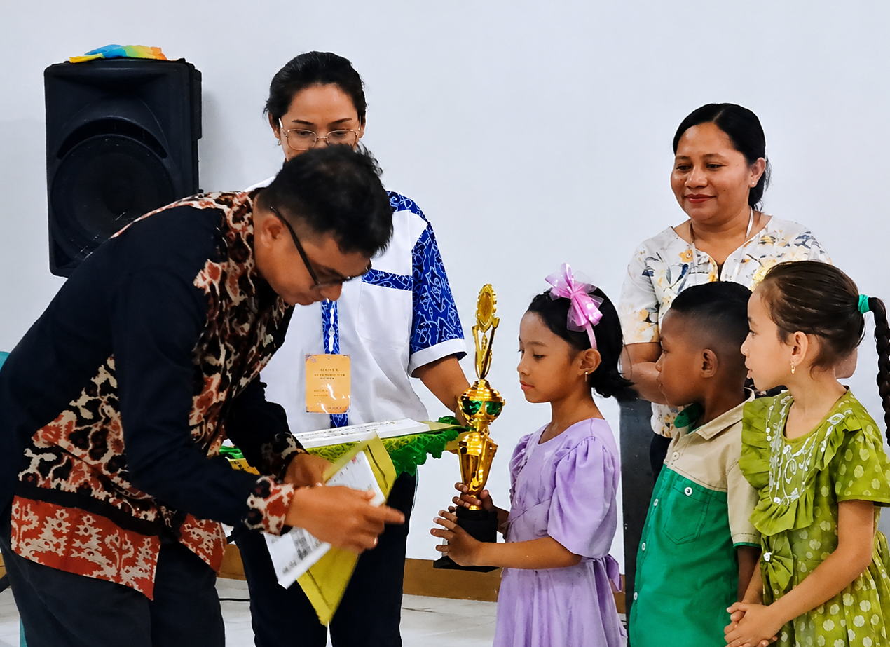 Ketua BPP Pendidikan Sinode GMIT, Pdt. Norman M. Nenohai, M.Si, menyerahkan hadiah uang tunai dan piala kepada Selena Neve Sandrine Gerimu, peserta juara 1 Lomba Solo Tingkat TK, Rabu (29/7) di Aula Pola Tribuana Kalabahi. (Foto: doc tribuanapos.net/dm).